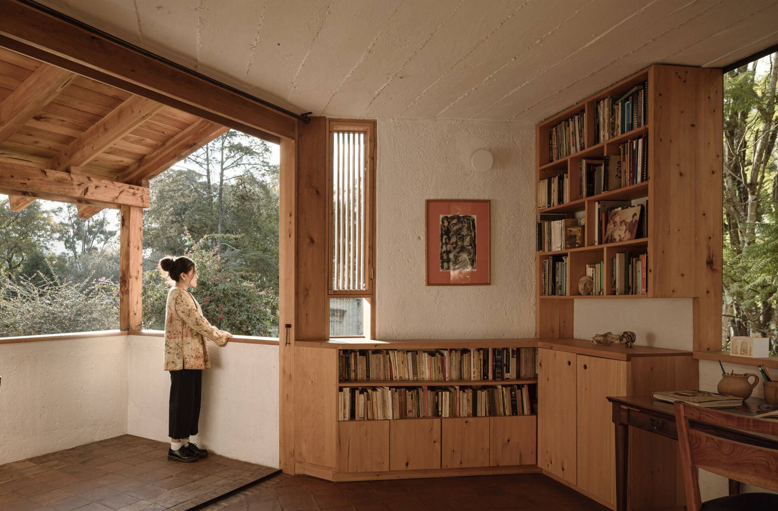 The upper-level study opens toward a covered terrace and the wooded surroundings.
