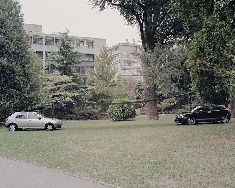 Two retired cars support a thin canopy on a lawn in It all remains